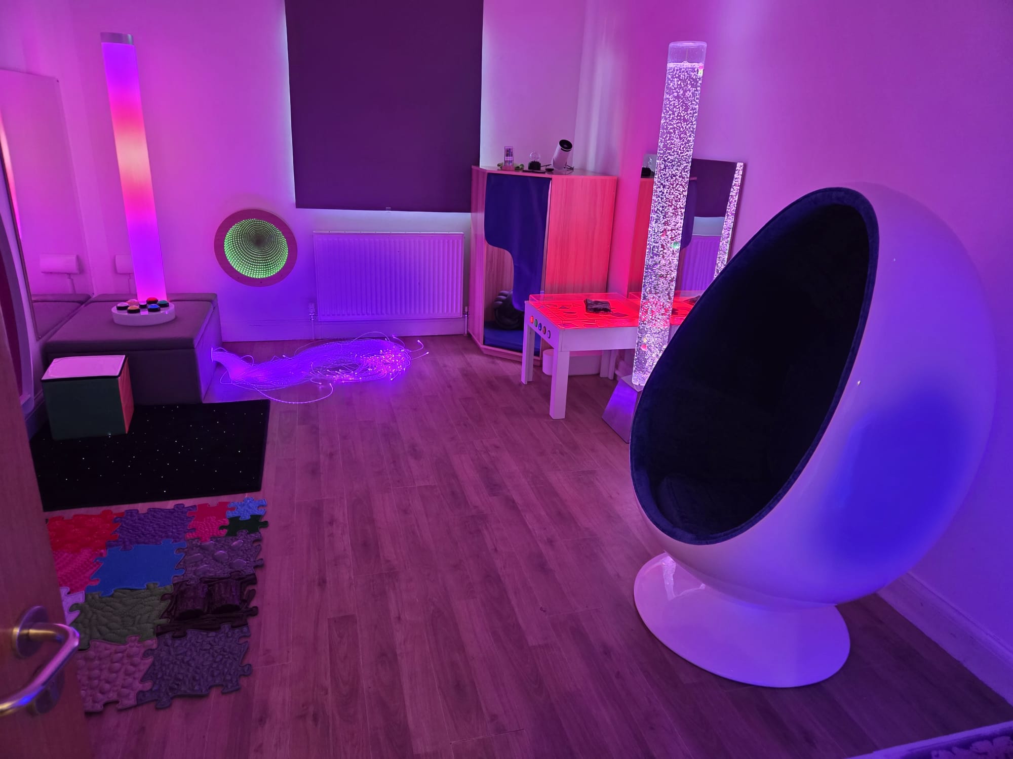 Saint Panteleimon Nursery School sensory room with a cocoon egg chair, bubble tube and tactile floor mats under soft purple light